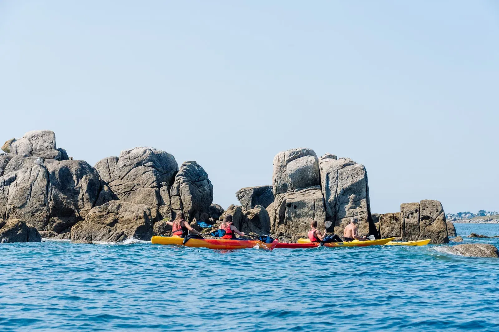 Sea kayaks weaving between granite rocks along the coast