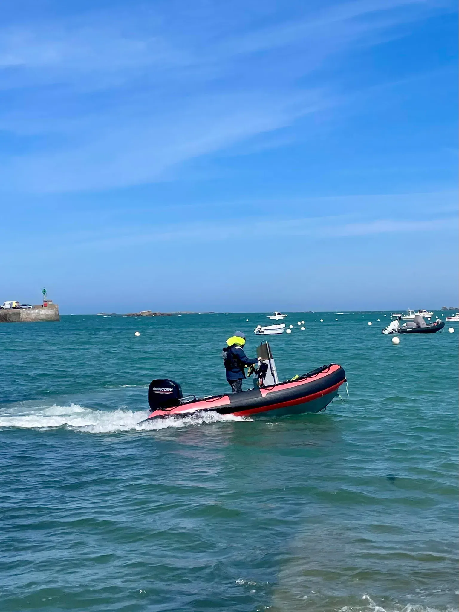 Moniteur debout à bord d'un semi-rigide rouge et noir, en approche du port de Roscoff